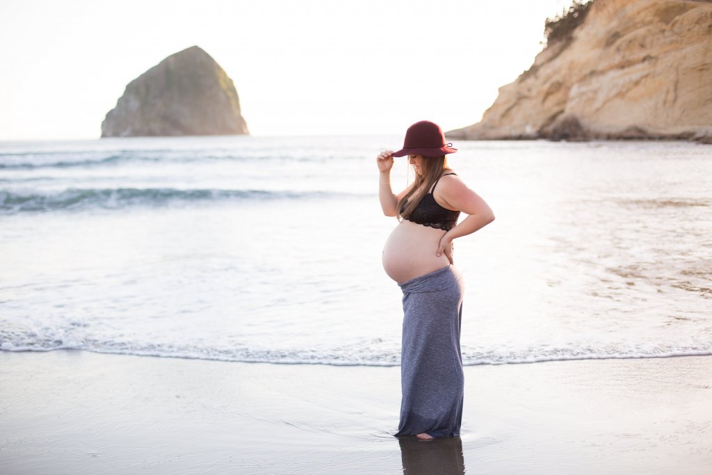 maternity photo shoot at the beach holding hat and back maternity photo shoot at the beach holding hat and back