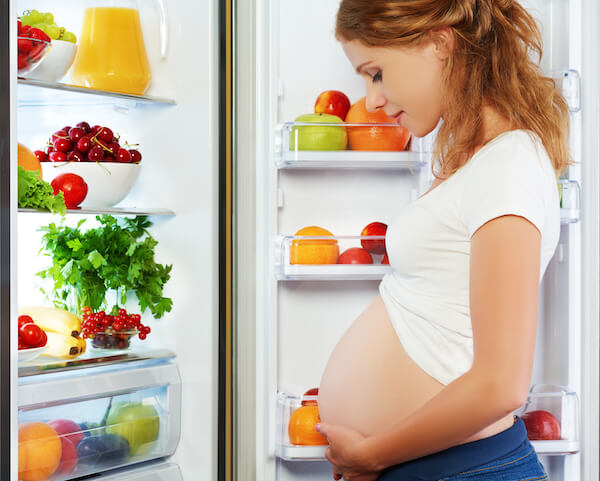 Pregnant woman standing by refrigerator Pregnant woman standing by refrigerator